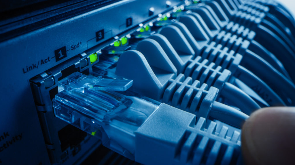 Clean network patching for stable connectivity Hands connect an Ethernet cable to a clean, labeled patch panel in a server rack.
