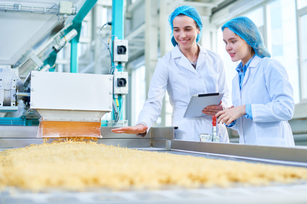 Conveyor of produce in a clean food plant with monitoring screens in the background.