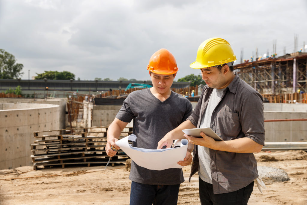 Foreman reviews digital blueprints on rugged tablet — Divine Logic Clean-shaven foreman in PPE checks blueprints on a rugged tablet at a jobsite.