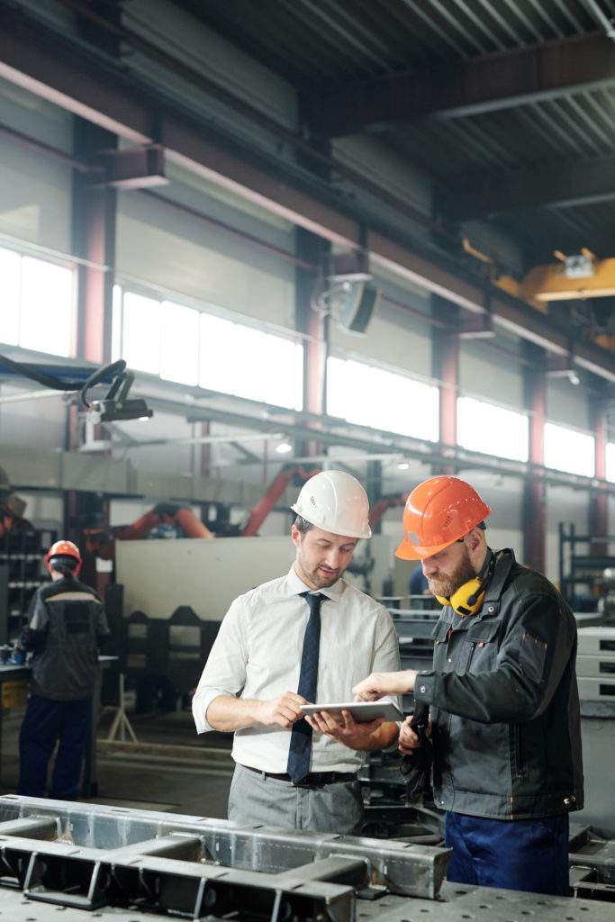 IT advisor and foreman collaborate on site — Divine Logic Clean-shaven IT technician advises a foreman on site using a laptop beside a steel frame.