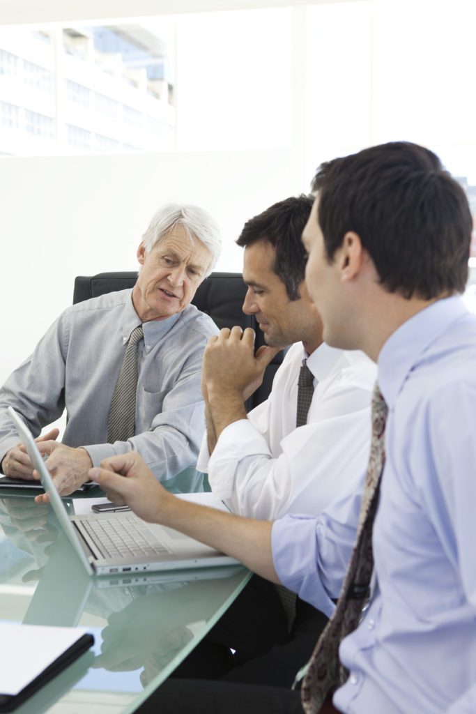 Divine Logic IT support planning for Fresno small businesses IT consultant in tie reviewing options with small-business owners around a laptop in a modern boardroom.