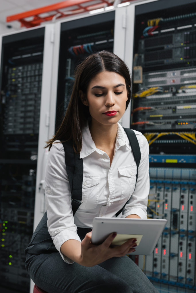 Proactive server check by local managed IT Clean-shaven technician in dress shirt reviews server racks with a tablet during a routine check.