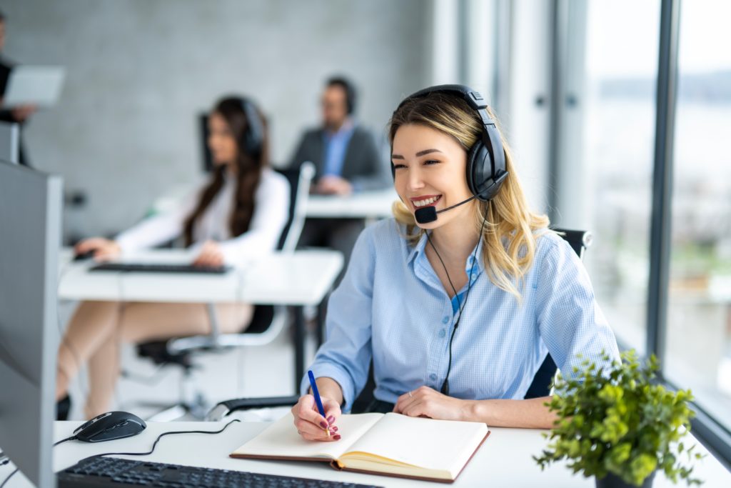 Professional helpdesk call—Divine Logic Business professional on a headset in a modern office with notepad ready.