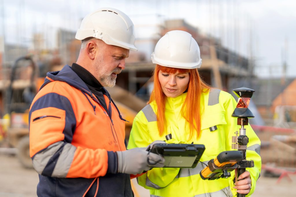 Rugged tablet in use at construction jobsite — Divine Logic Gloved hands hold a rugged tablet with construction equipment in background.